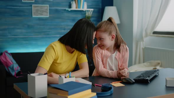 Affectionate Mother Sitting at Desk with Daughter for Homework