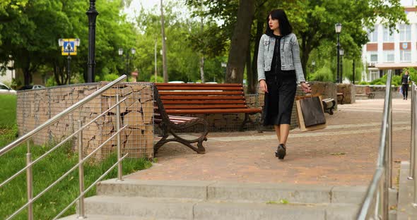 Woman holding several paper bags walking outdoors in the park