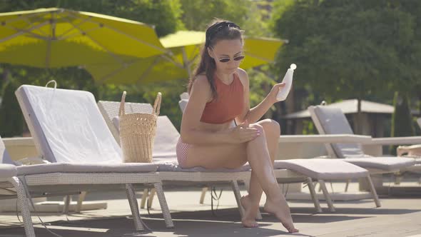 Wide Shot of Beautiful Young Woman Applying Skin Suntan Cream on Legs and Smiling. Portrait of