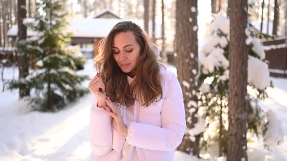 Winter Sunny Cold Portrait in Snowfall of Beautiful Young Woman in a White Warm Outwear Down Jacket