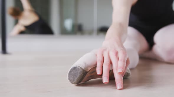 Caucasian female ballet dancer stretching up on the floor for dance class in a bright studio
