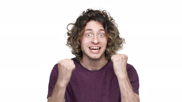 Portrait of Happy Guy with Curly Hair in Casual Tshirt Rejoicing and Clenching Fists in Surprise