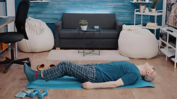 Senior Man Raising Legs to Do Gymnastics on Yoga Mat