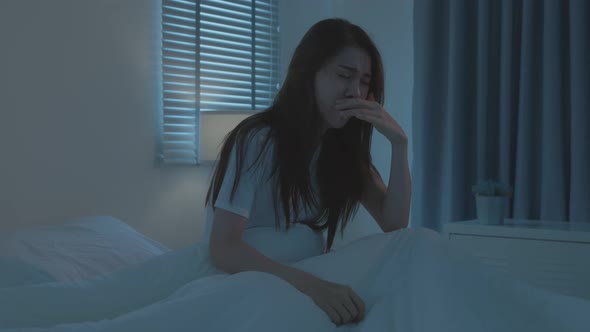 Asian beautiful girl in pajamas feeling sick with fever and coughing while sit on bed in bedroom.