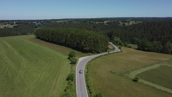 Car drives through road in nature reserve Eifel in Germany, hills and forest