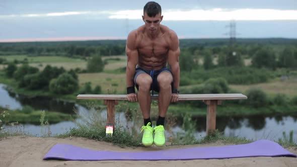 A Young Athlete in Blue Shorts Does a Handstand on a Bench By the River and Shakes the Press By