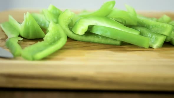 Slicing green bell pepper on a wood cutting board.