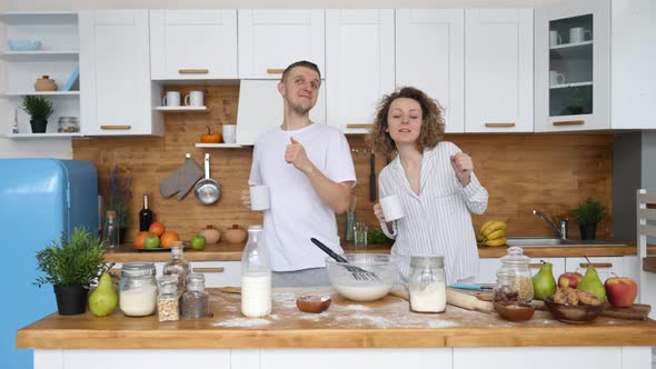 Young Couple With Coffee Cups Dancing Together In Kitchen While Cooking Breakfast.