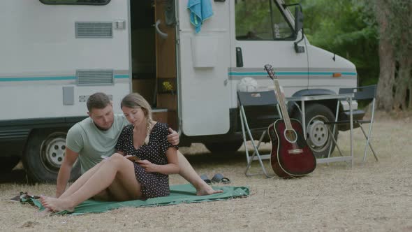 Lovely couple sitting together and reading a book against motor home RV campervan