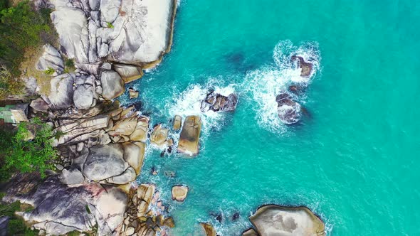 Rocky coast with exotic vegetation and houses on the cliff edge. Turquoise sea water and foamy waves