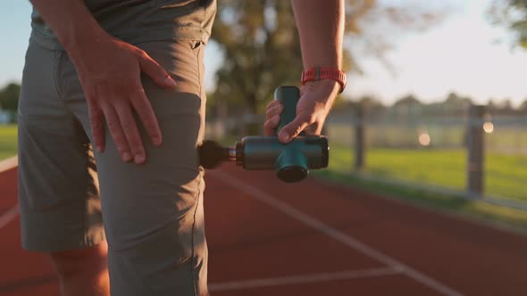 Athletic Male Massages Muscles with Hand Massage Gun Recovering From Stadium Running Workout