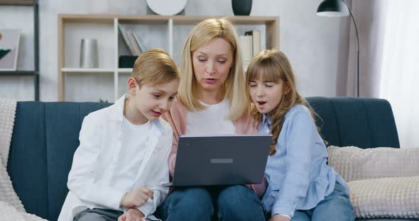 Family of Mother and Two Kids which Sitting Together on the Soft couch at Home and Use Computer