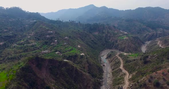 A river between the mountains and a road is with the river. A green hills view from drone.