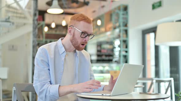 Shocked Expression By Redhead Man Using Laptop in Cafe 