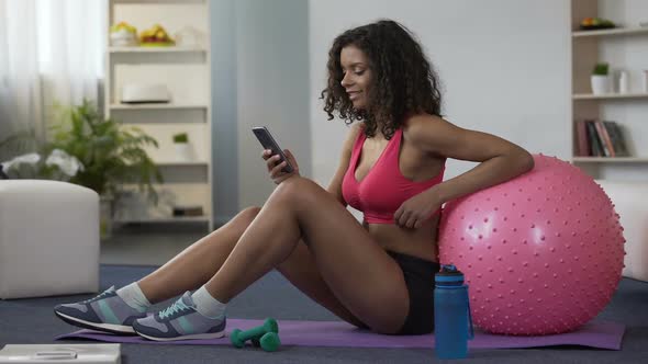 Biracial Woman in Gym Outfit Sitting on Floor, Using Mobile Phone, Application