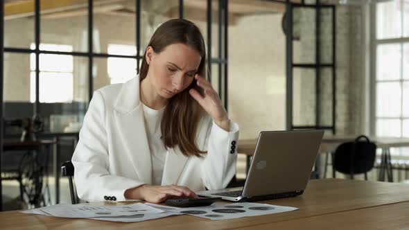 Stylish Young Female Accountant Looking Through Finances Using a Laptop and a Calculator