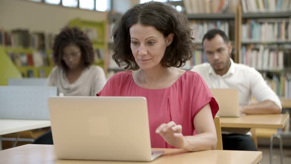 Thoughtful Curly Mature Woman Working with Laptop at Library