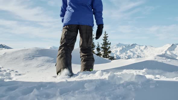 Boy in snowboard outfit walking through the snowdrift in the alpine scenery.