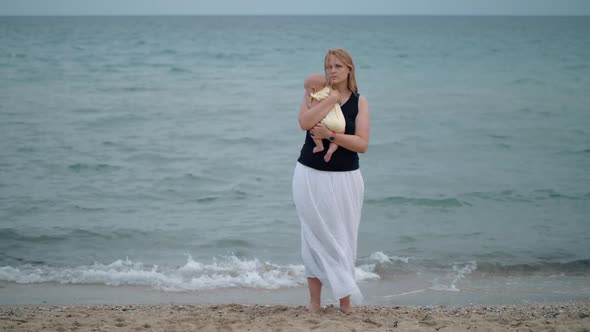  - Mother with Lost Look Holding Baby Being Alone at the Beach Near Sea