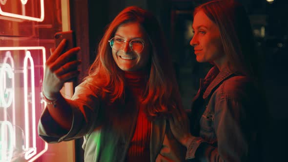 Two Millennial Women Pose on Phone Camera in Neon