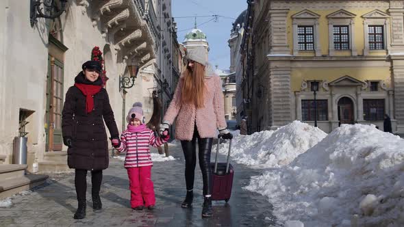 Sisters Tourists Travelers Walking with a Suitcase on Snowy City Street Enjoying Time Together