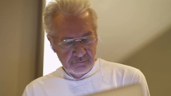 Handheld Portrait of an Elderly Grayhaired Man with Glasses Looking at a Laptop Screen a Focused Man