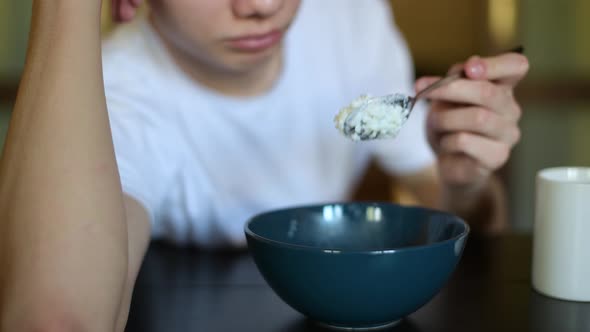 plate with rice porridge. Teen lazily picking porridge with a spoon