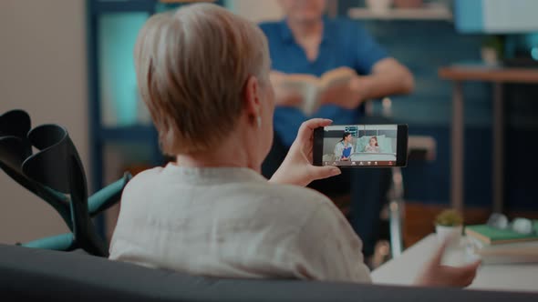 Old Woman with Crutches Using Video Call on Mobile Phone