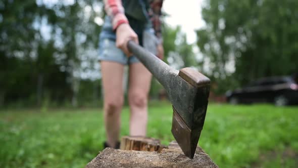 A woman sticks an ax into a piece of wood. Close-up