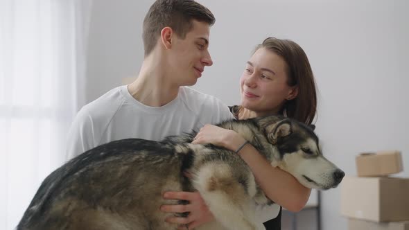 A Happy Young Married Couple Hold a Cute Husky Dog in Their Arms in a New Spacious Apartment