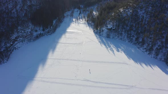 Aerial top down view single person ice skating on frozen lake - Wide Snowy Landscape