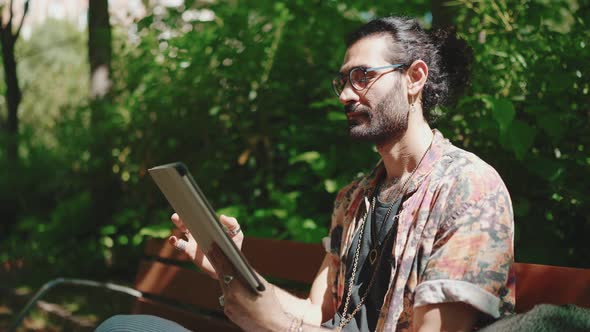 Concentrated curly-haired bearded man in eyeglasses looking at tablet