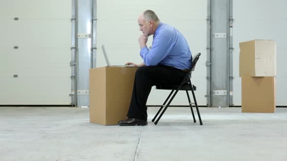 Business man in warehouse with laptop on cardboard box