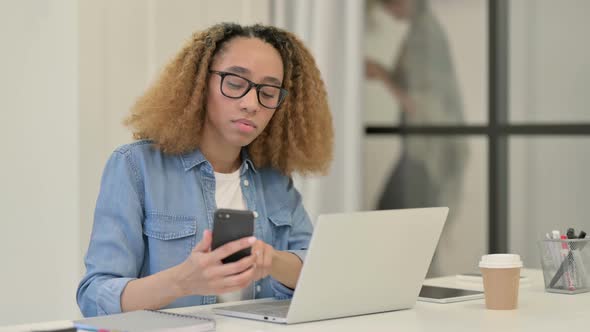 African Woman Working on Smartphone and Laptop in Office