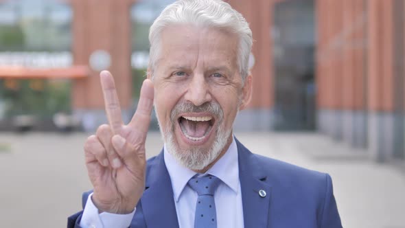 Sign of Victory by Old Businessman Standing Outdoor