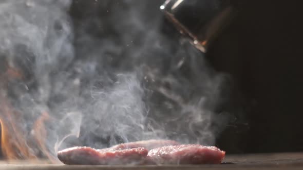 Grilled Meat Steak. Cooking on Fire. Slow Motion Beef Steak Close-up. The Cook Sprinkles Meat with