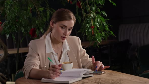 A Beautiful Blonde Girl Drinks Coffee and Writes in a Notebook