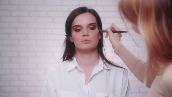 Makeup Artist Using a Palette for Applying Pinky Gloss Onto a Model's Face