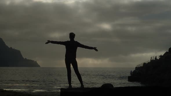 Silhouette of a Woman at Sunset Raising Arms in the Air Observing Waves and Dramatic Thunderstorm