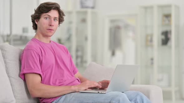 Young Casual Man with Laptop Smiling at Camera at Home