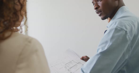 Biracial male and female architects checking architects plans in modern office