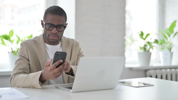 African Man Using Smartphone While Using Laptop in Office