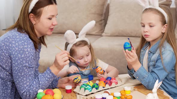 Mom and Daughters with Rabbit Ears Decorate Easter Eggs with Paints