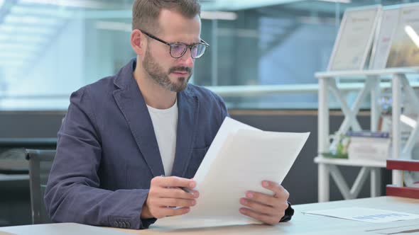 Middle Aged Businessman Reading Documents While Sitting in Office