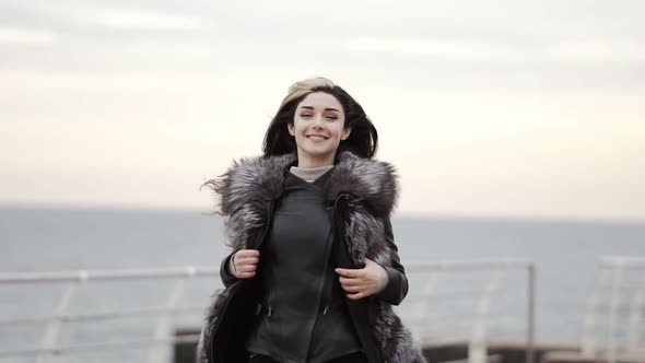 Portrait of a Young Brunette Woman in Fur Coat Running By the Sea or Ocean in Winter Turning Around