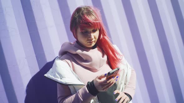 Independent Young Woman with Pink Hair Uses Smartphone on Purple Containers Background