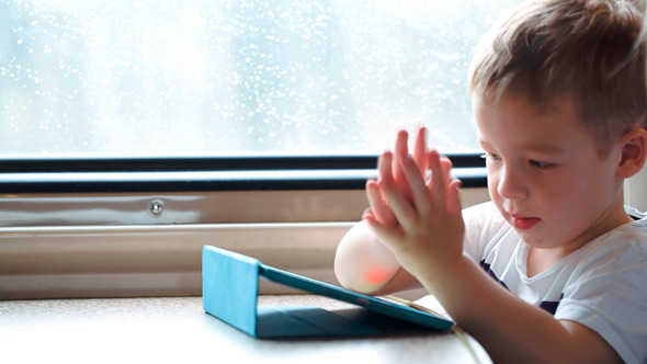 Boy Playing On Pad In The Train Trying To Win