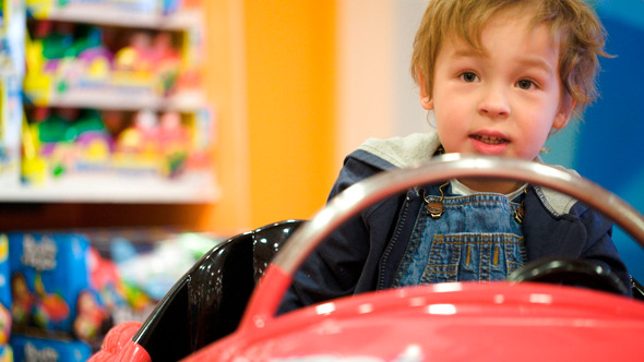Little Boy Swinging In A Toy Car In The Shop