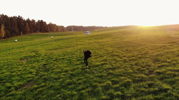 Aerial View of a Young Girl Spinning with Arms Outstretched in the Sunset on a Large Green Field