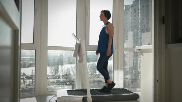 Woman is walking on running machine at home. 